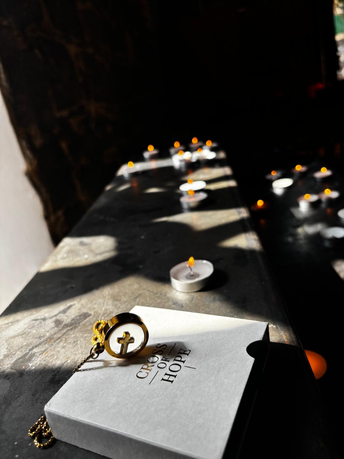 Book titled 'Credo of Hope' with a cross pendant on a dark surface with candles in the background.