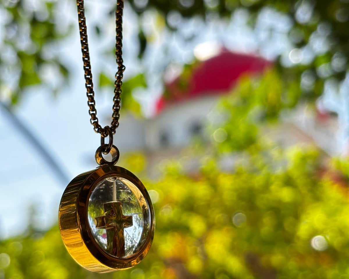 Necklace with a round pendant featuring a cross, blurred green foliage in the background