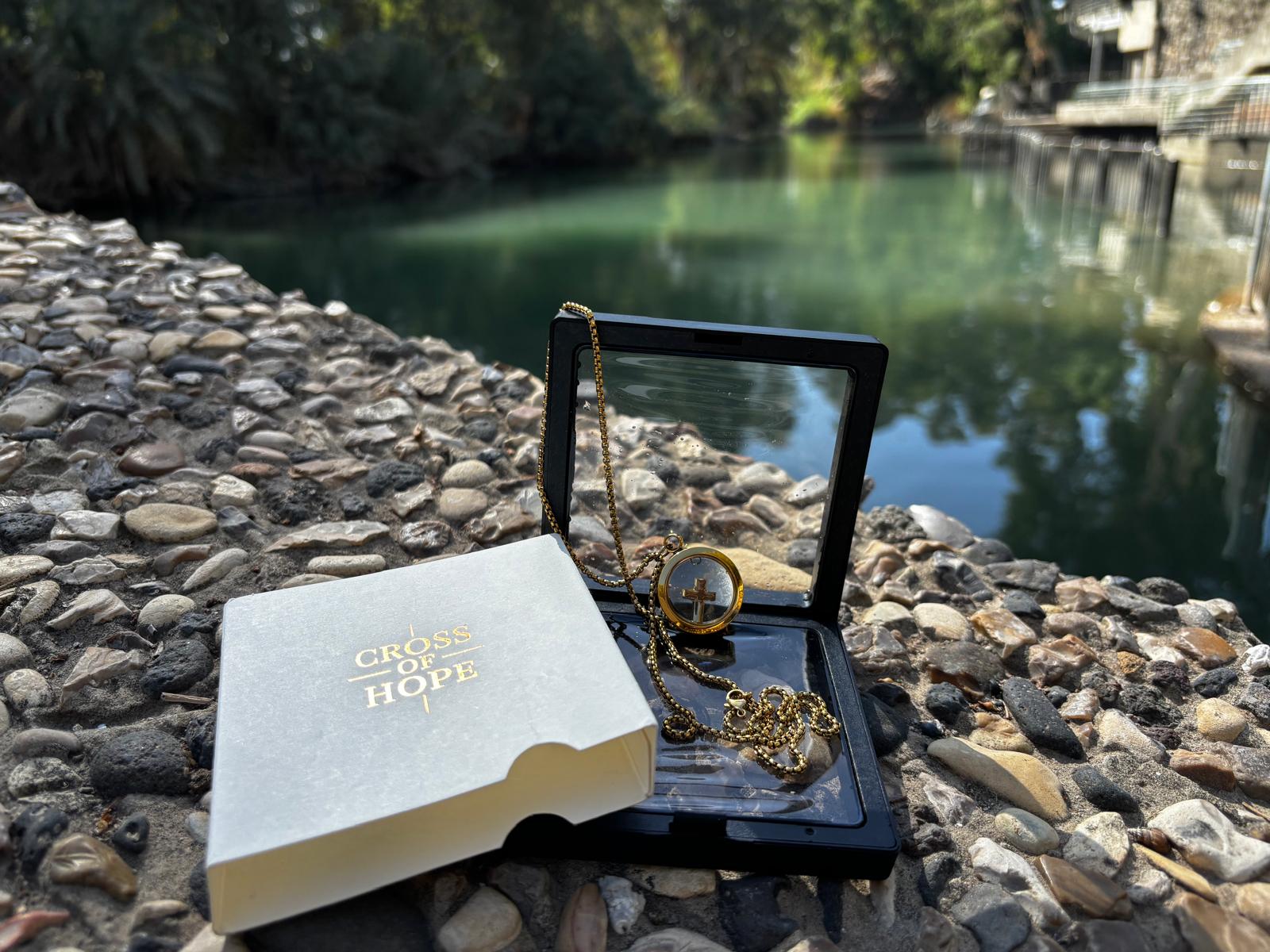 Open jewelry box with necklace on a stone surface near a body of water